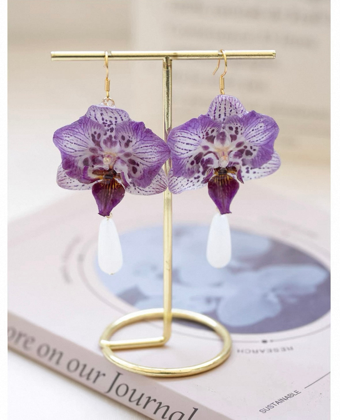 Purple teardrop orchid earrings with resin petals on a gold-tone display by Terra Decode