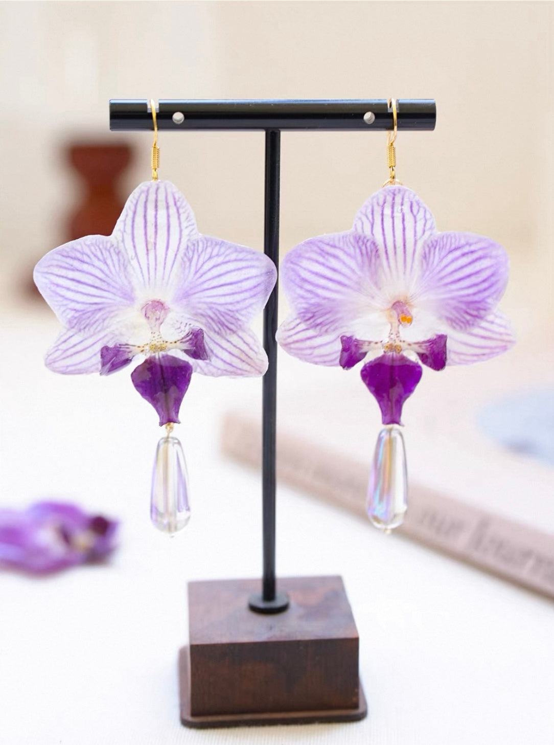 Soft purple orchid drop earrings with resin petals and clear teardrops on a display stand by Terra Decode