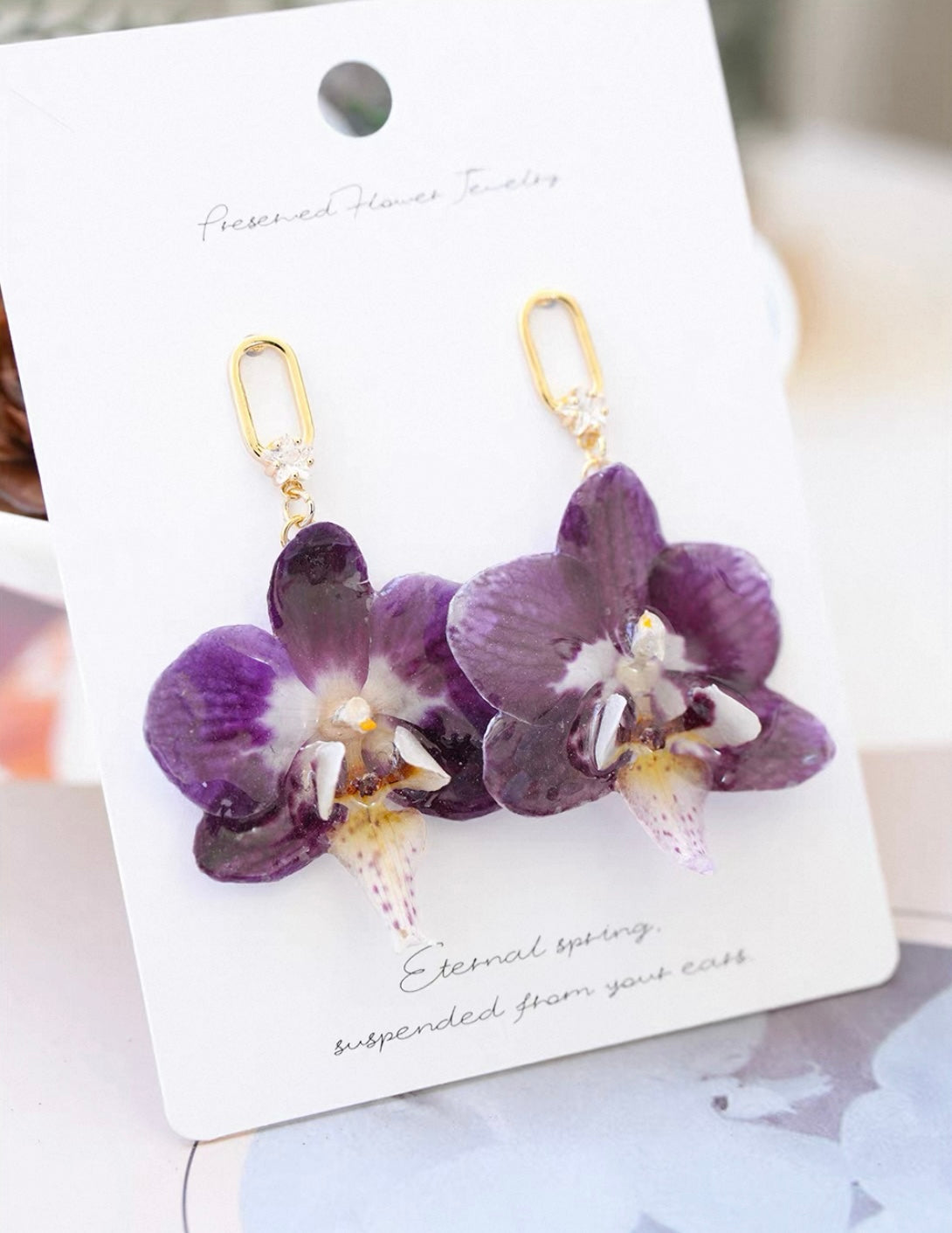 Purple orchid hook earrings with resin petals and gold-tone links on a jewellery card by Terra Decode