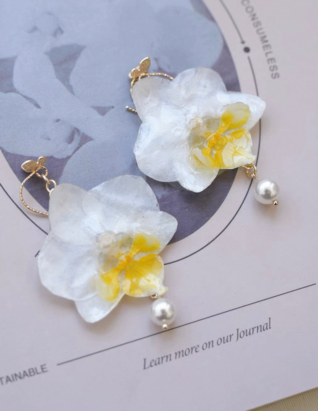 Cream white orchid pearl drop earrings with resin petals on a printed card by Terra Decode