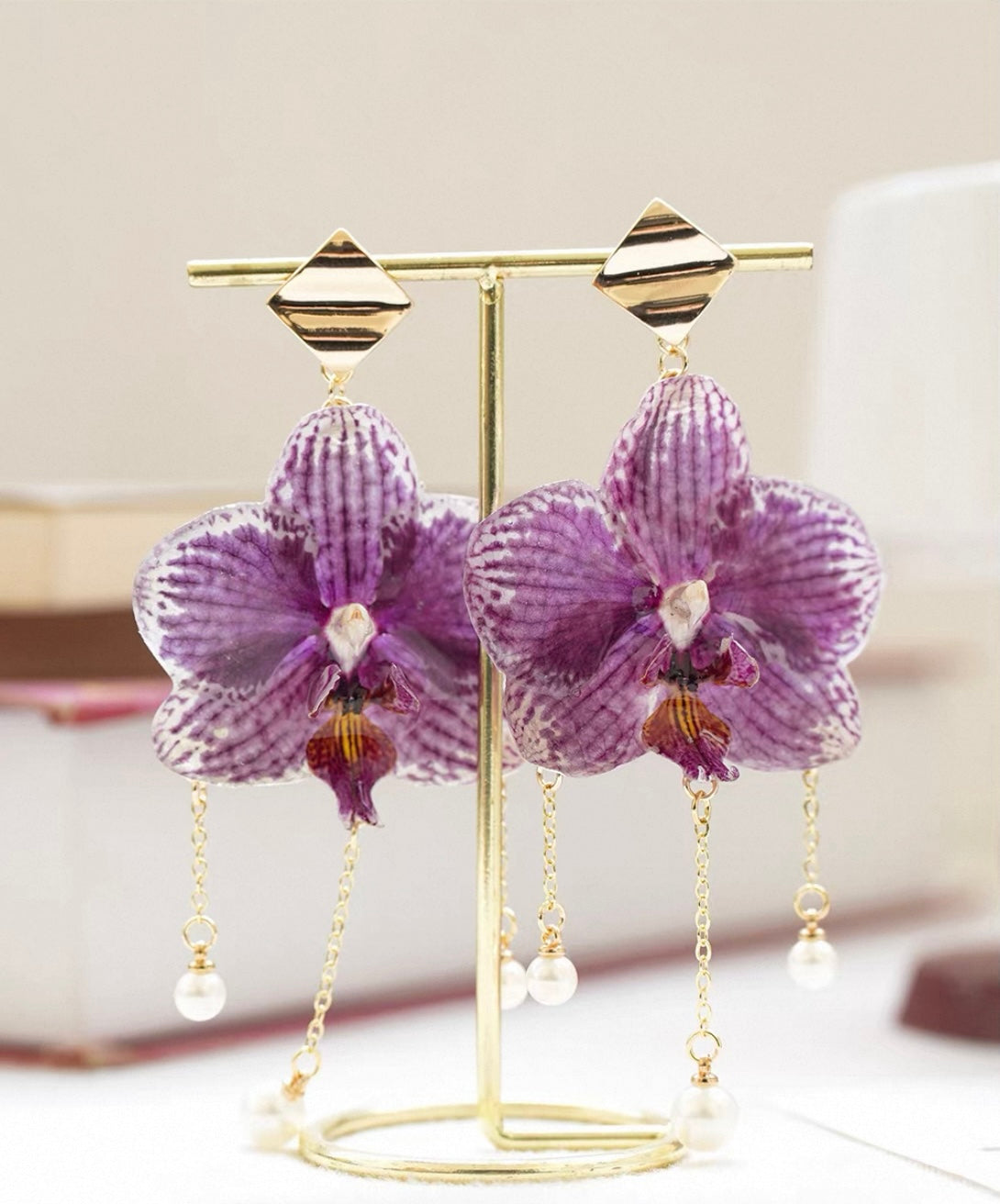 Purple orchid earrings with resin flower petals on a gold-tone display stand by Terra Decode