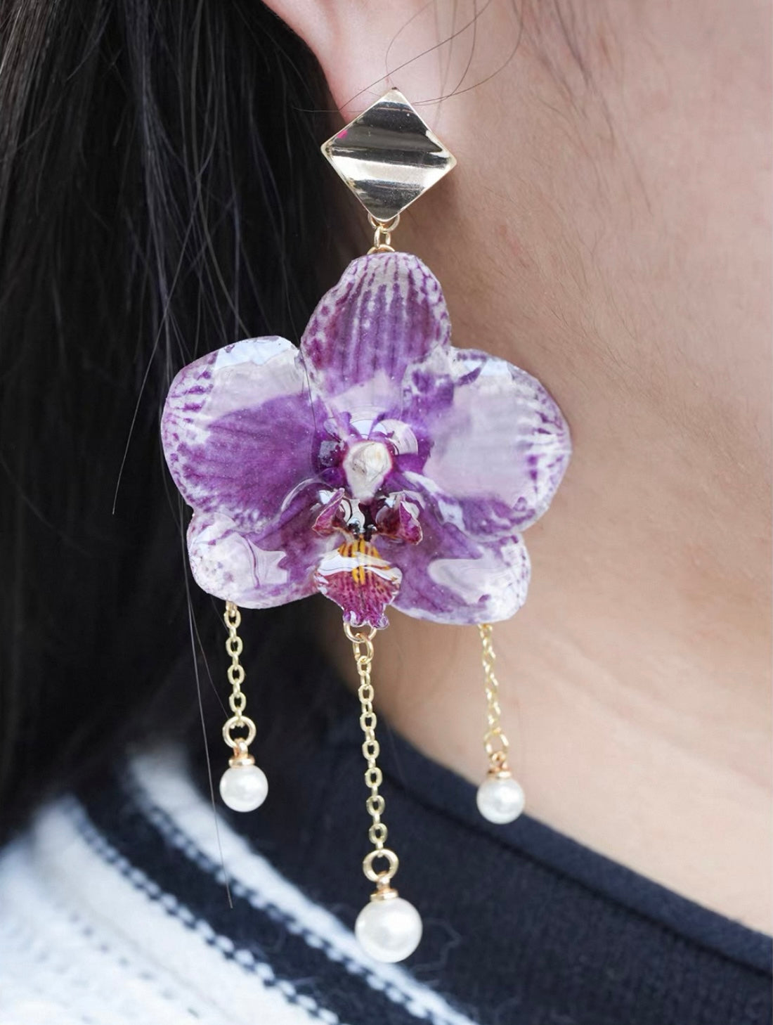 Purple orchid earrings with resin petals and pearl-like drop worn on ear by Terra Decode