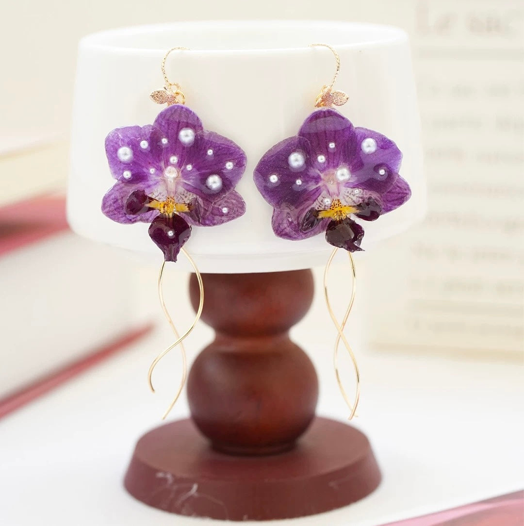 Purple orchid earrings with resin petals beside lamp and book styling by Terra Decode