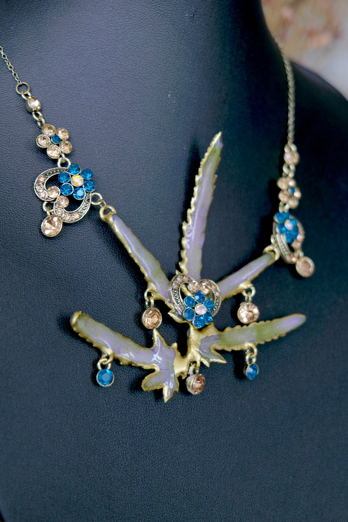 Detail of the preserved Lygodium japonicum leaf necklace with blue crystal floral accents and antique-gold metalwork.