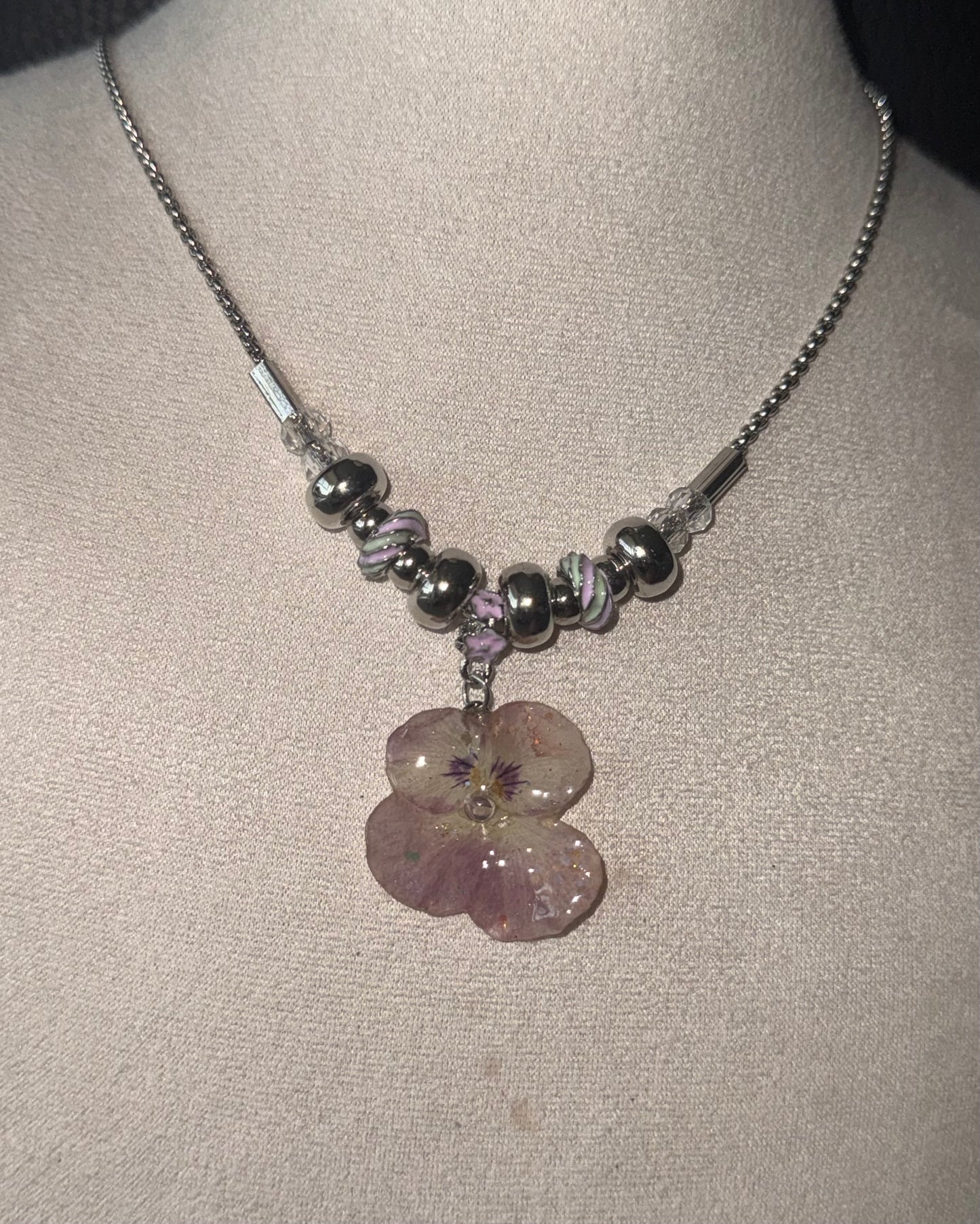 Reflective detail of smoky-pink pansy pendant and pink-lilac swirl beads