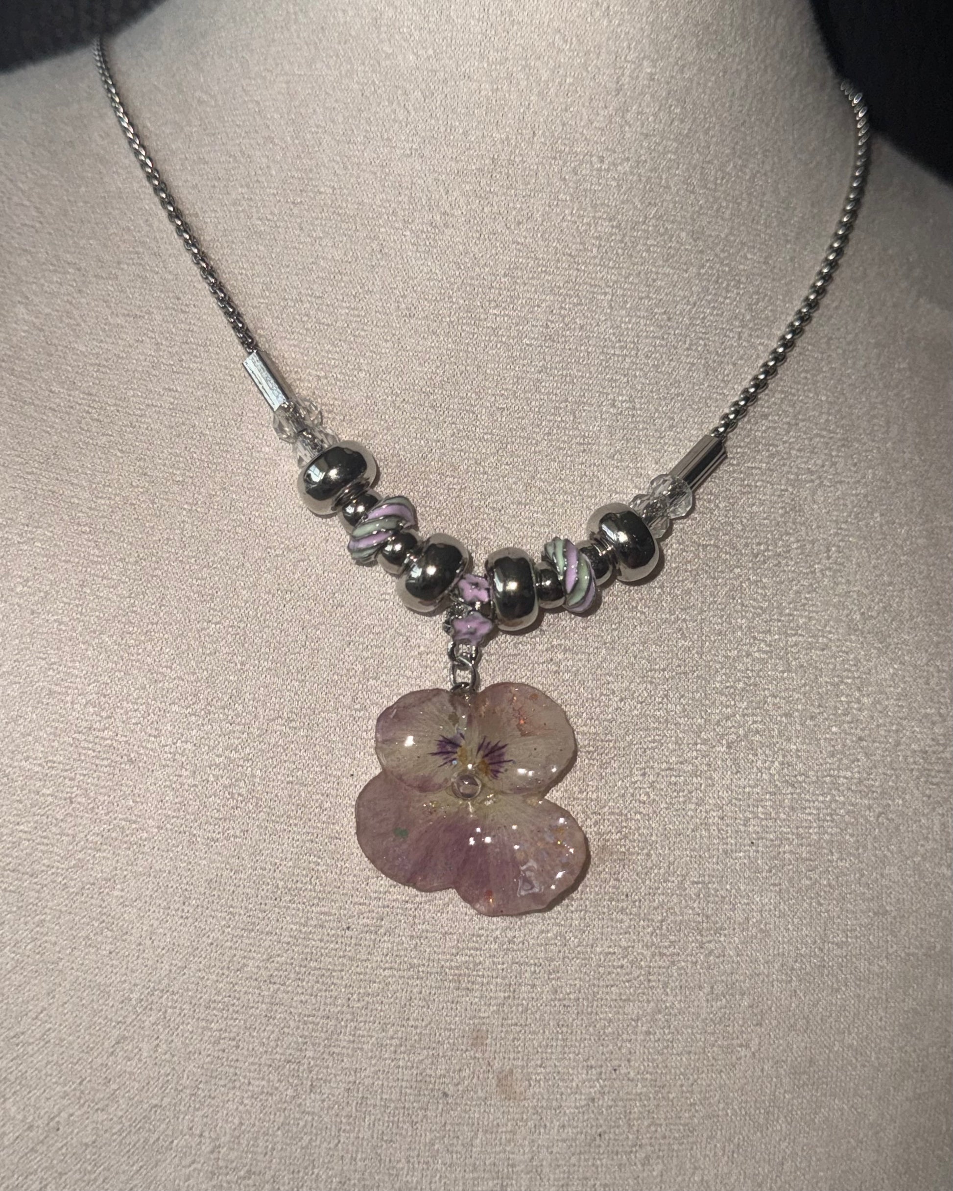 Reflective detail of smoky-pink pansy pendant and pink-lilac swirl beads