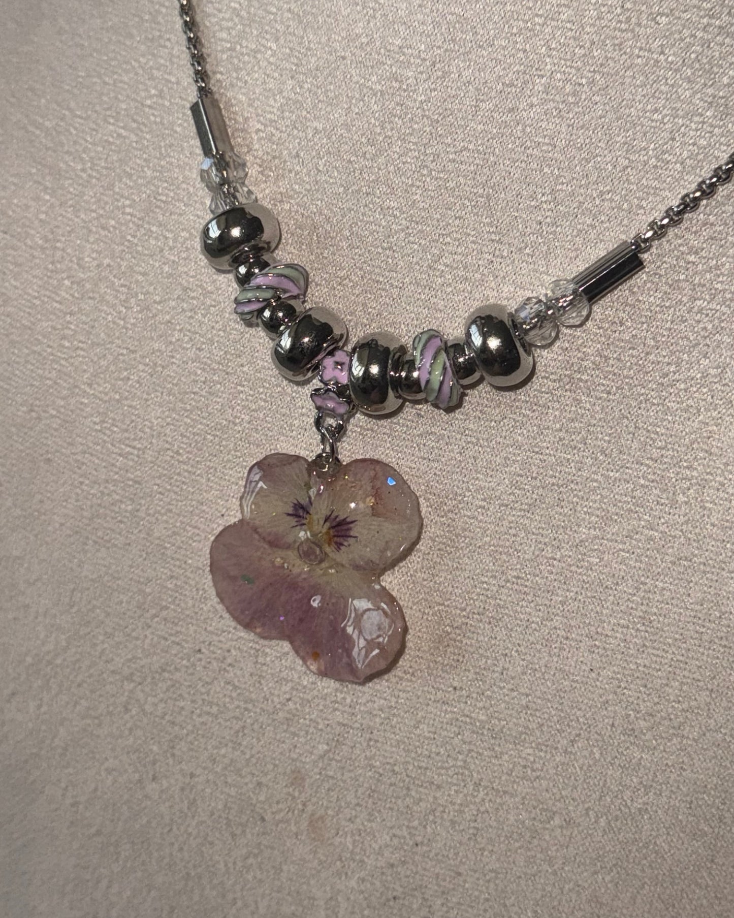 Close-up of smoky-pink pansy resin pendant with silver-toned rounded beads