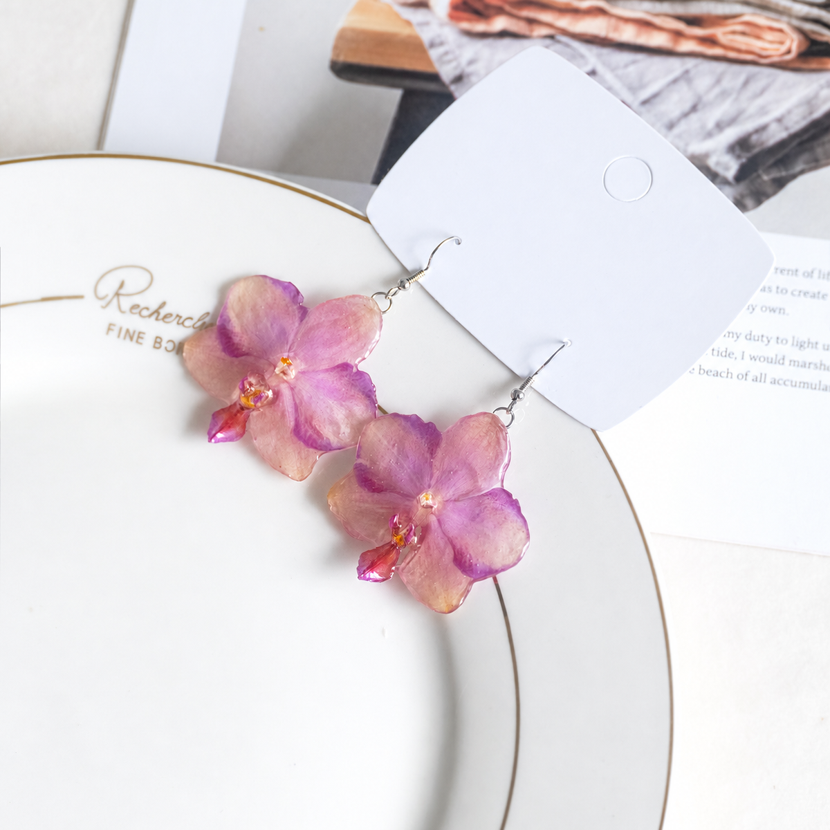 Angled view of two preserved orchid earrings beside a blank display card, Sunset Pink Phalaenopsis Drop Earrings botanical jewellery by Terra Decode