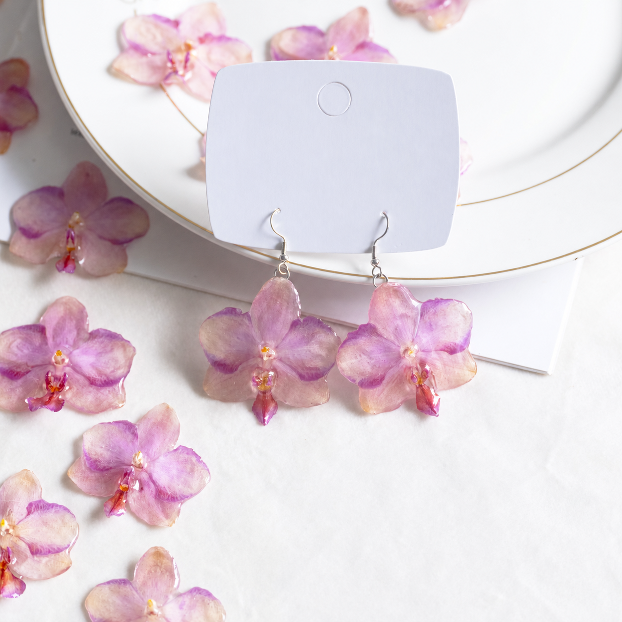Botanical flat lay of the orchid earring pair surrounded by matching resin flowers, Sunset Pink Phalaenopsis Drop Earrings botanical jewellery by Terra Decode