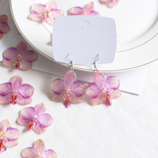 Botanical flat lay of the orchid earring pair surrounded by matching resin flowers, Sunset Pink Phalaenopsis Drop Earrings botanical jewellery by Terra Decode