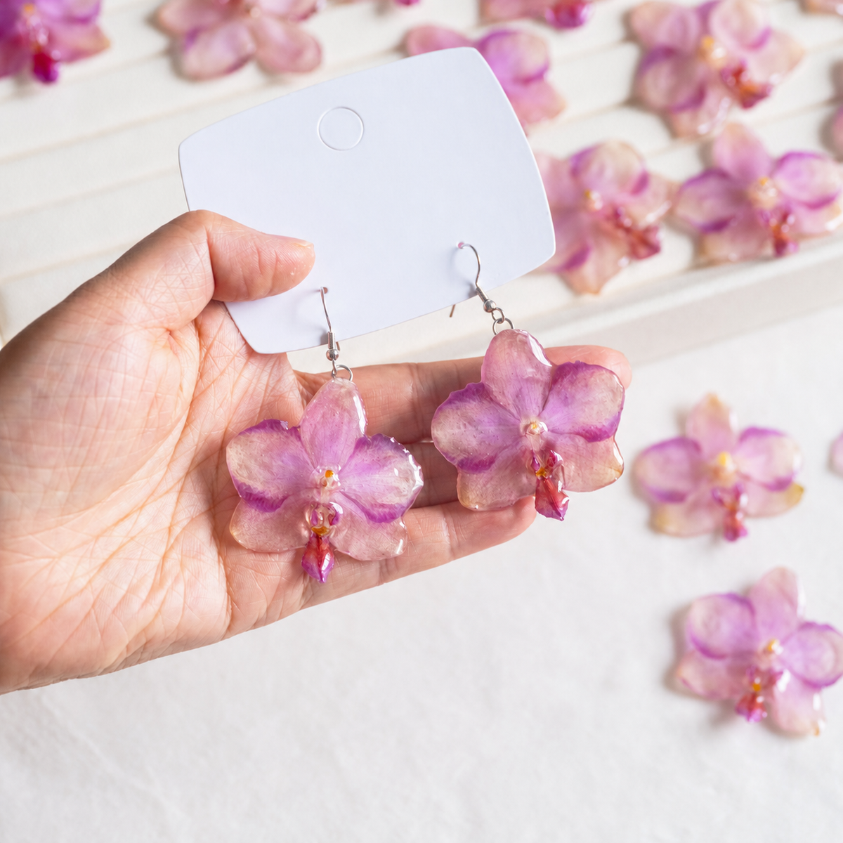 Hand-held view showing the scale of the pink-purple orchid drop earrings, Sunset Pink Phalaenopsis Drop Earrings botanical jewellery by Terra Decode