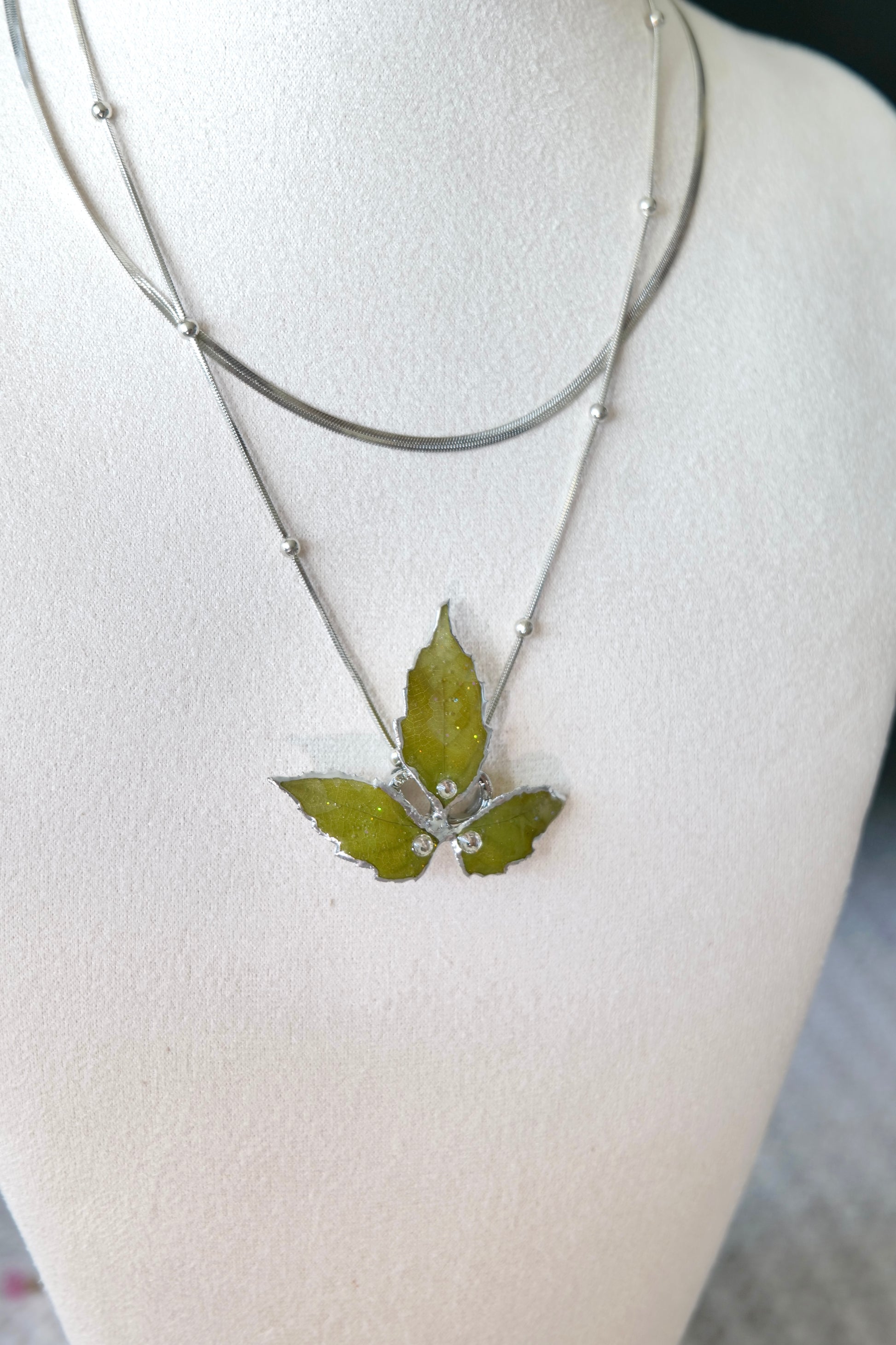 Left angled view of the layered silver three-leaf botanical necklace by Terra Decode
