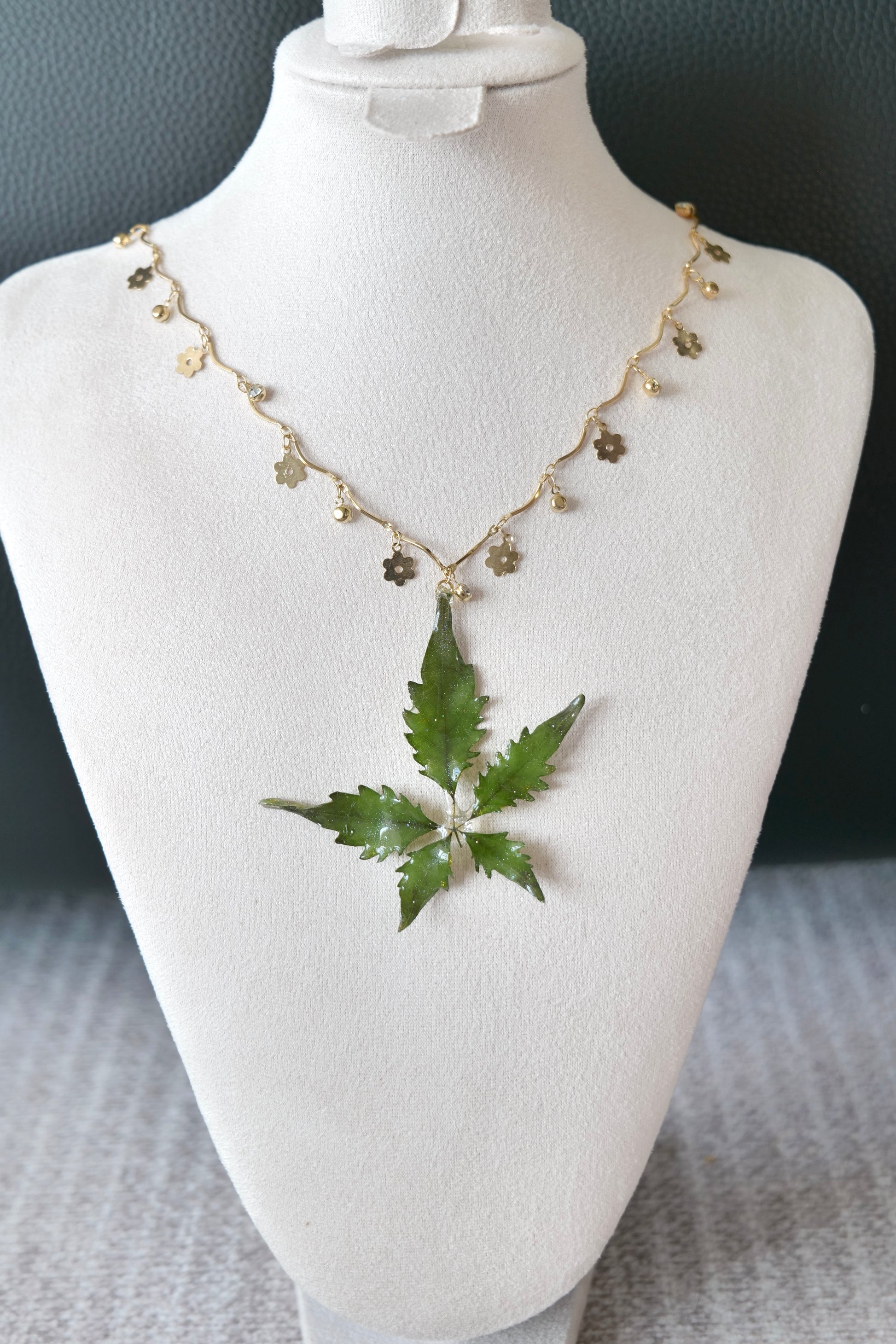Left angled view of the serrated five-leaf floral-charm necklace by Terra Decode
