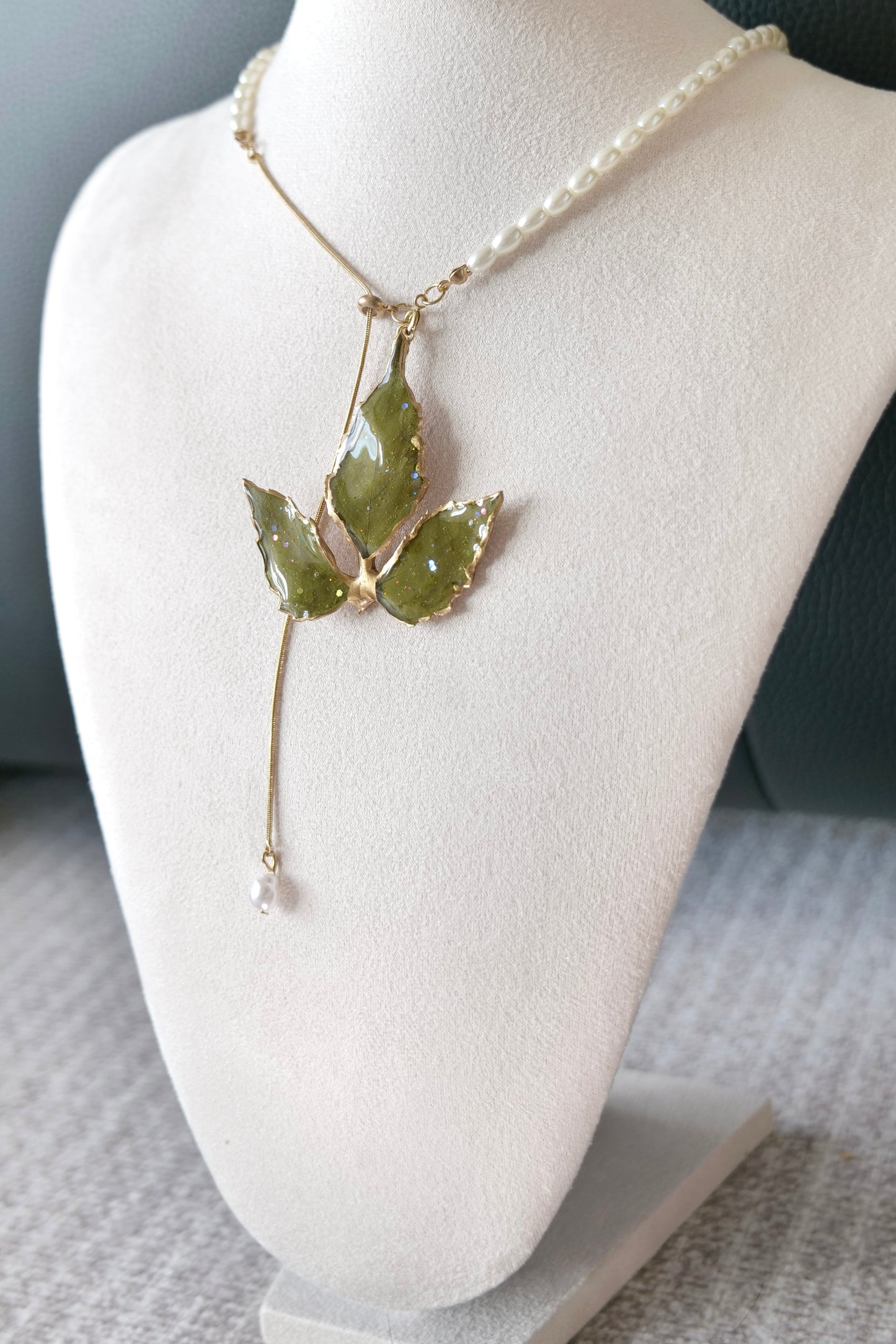 Left angled view of the gold-edged broad three-leaf pearl-drop necklace by Terra Decode