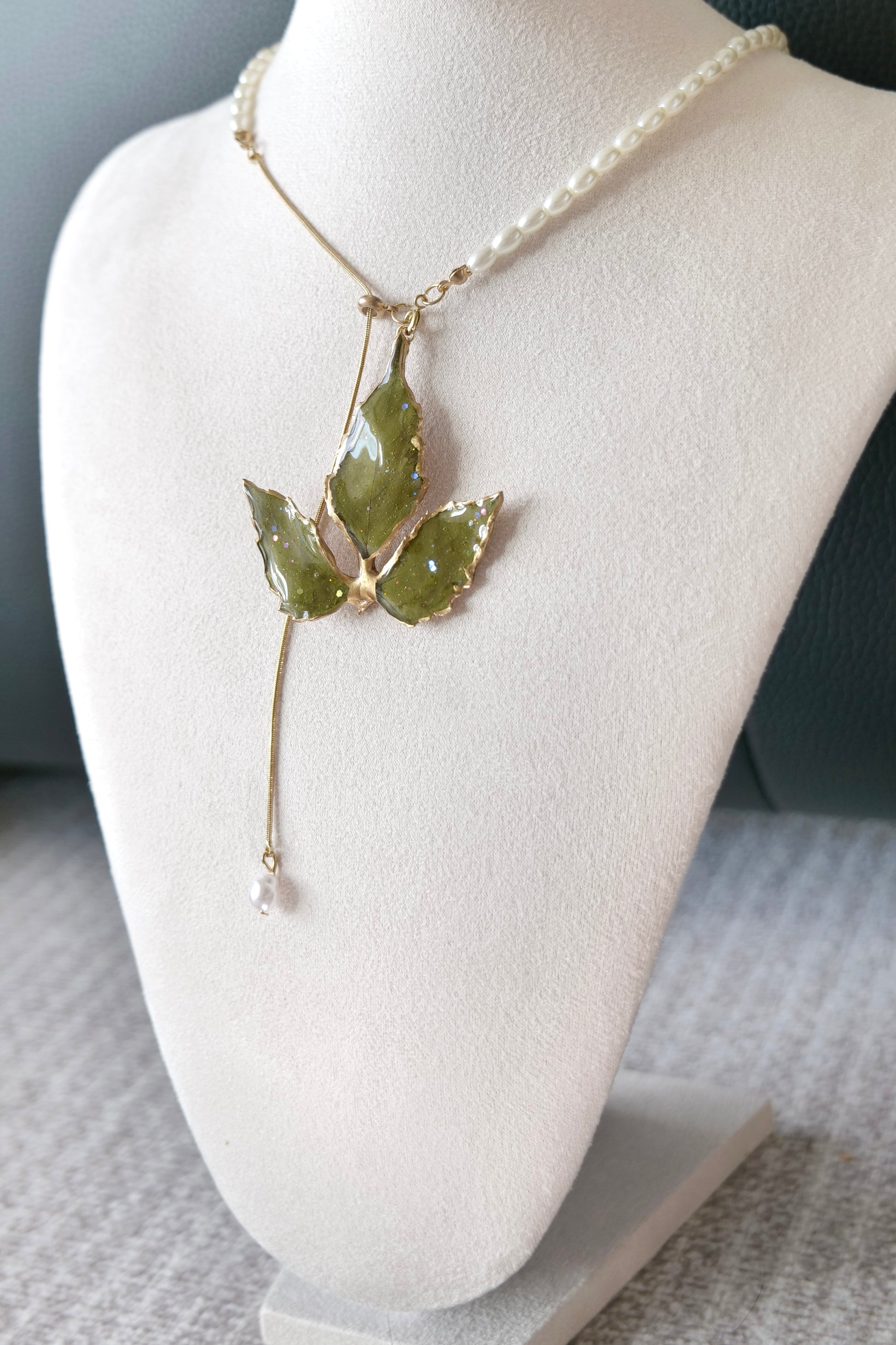 Left angled view of the gold-edged broad three-leaf pearl-drop necklace by Terra Decode