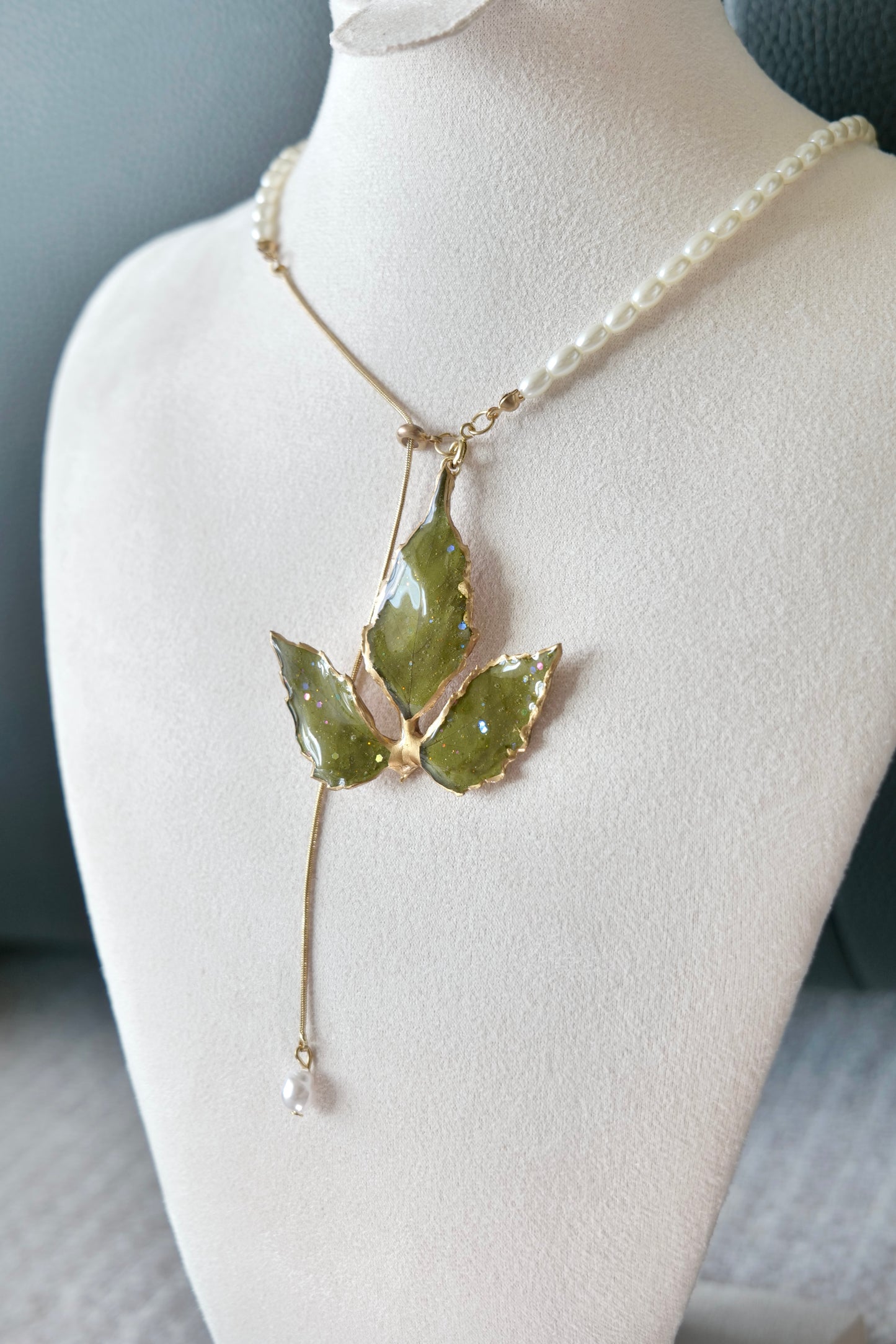 Right angled view of the gold-edged broad three-leaf pearl-drop necklace by Terra Decode