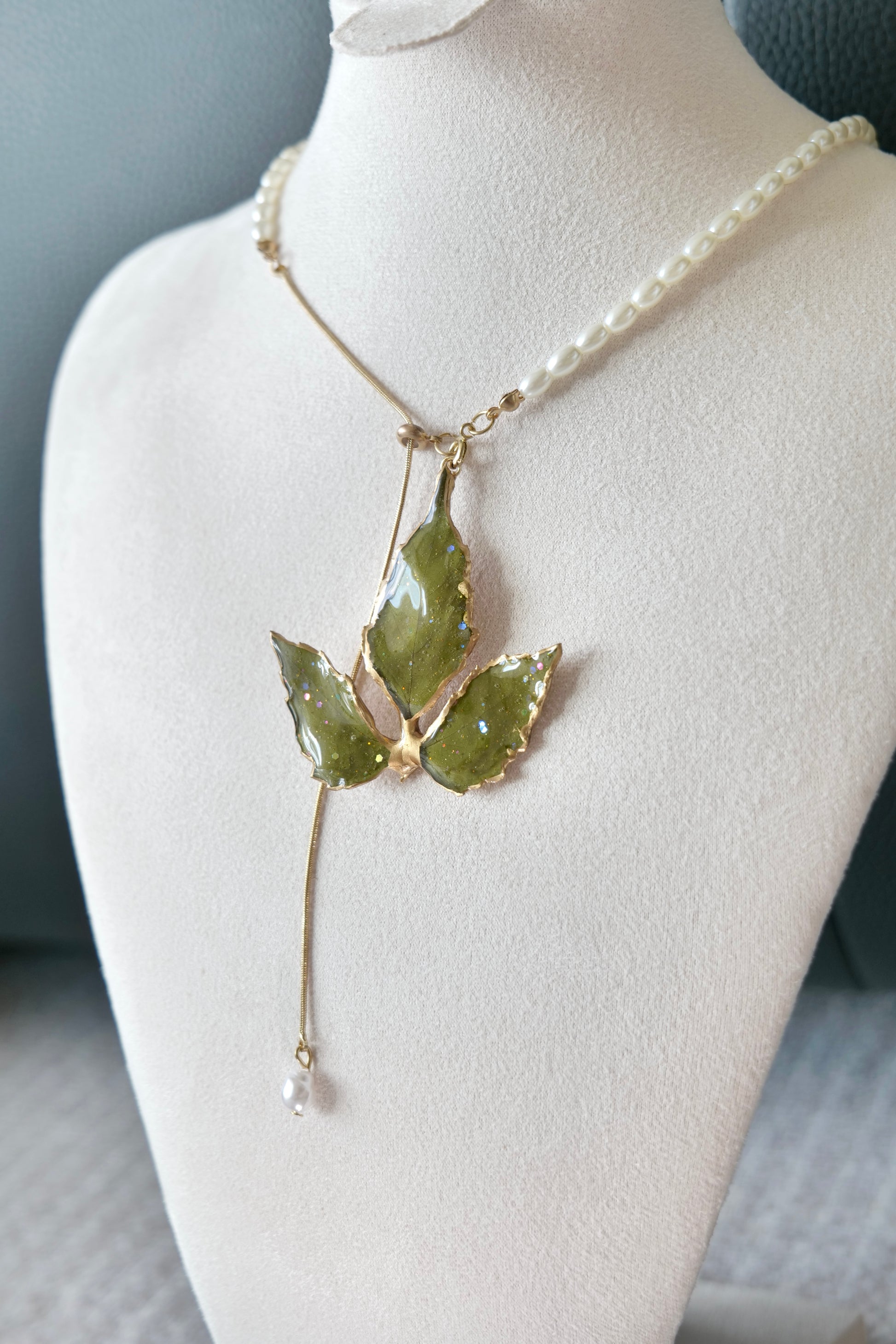 Right angled view of the gold-edged broad three-leaf pearl-drop necklace by Terra Decode