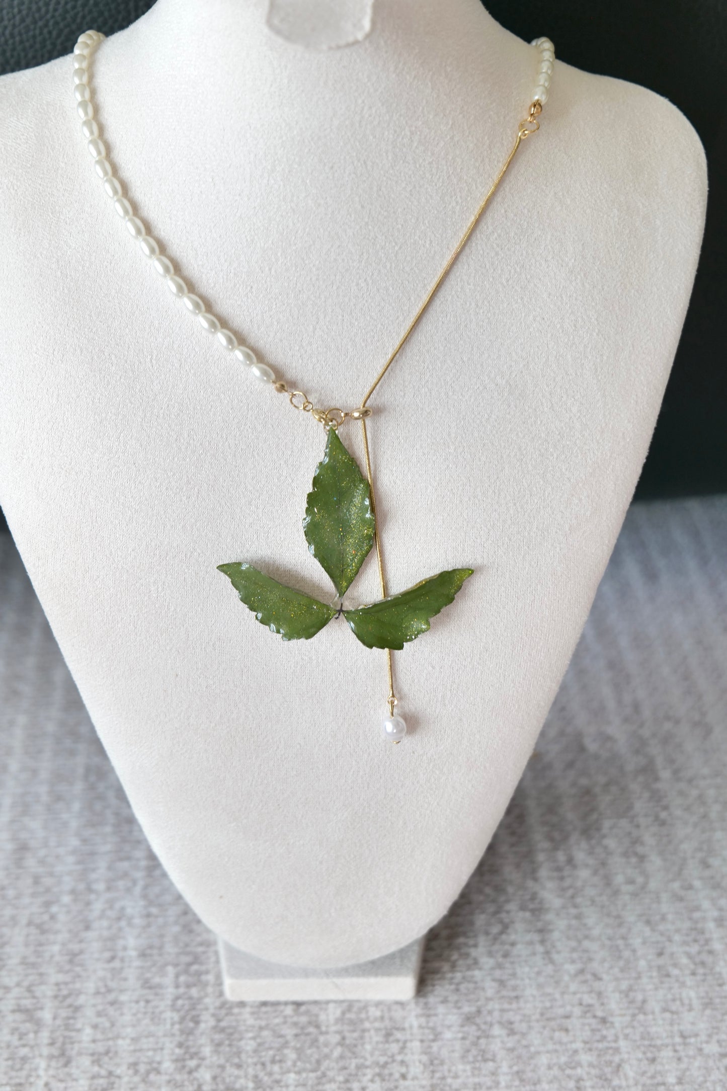 Left angled view of the minimal olive three-leaf pearl-drop necklace by Terra Decode