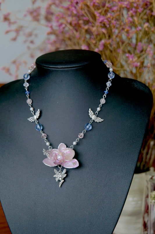 Detail of a pink Phalaenopsis orchid necklace with angel wing charms, blue beads and pearl accents.