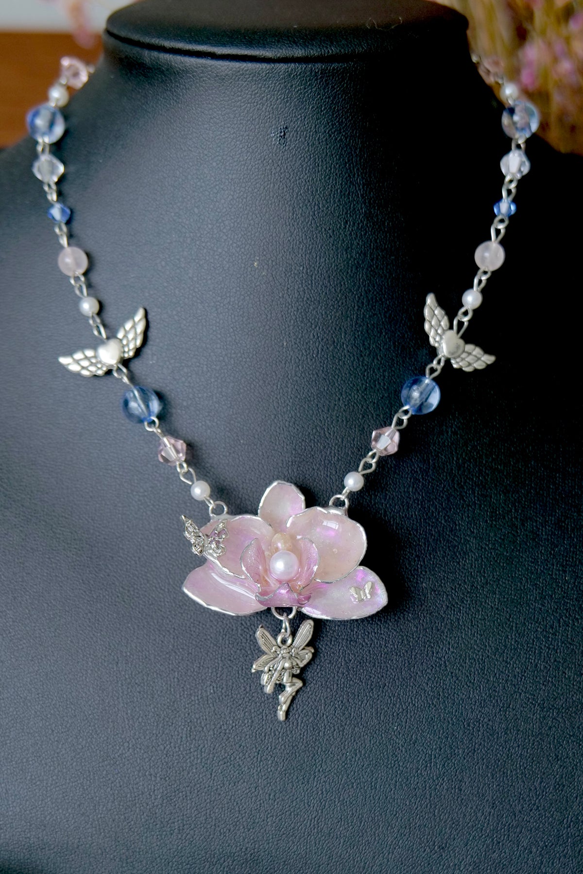 Close-up of a pink preserved Phalaenopsis orchid pendant with pearl centre and silver angel charm.