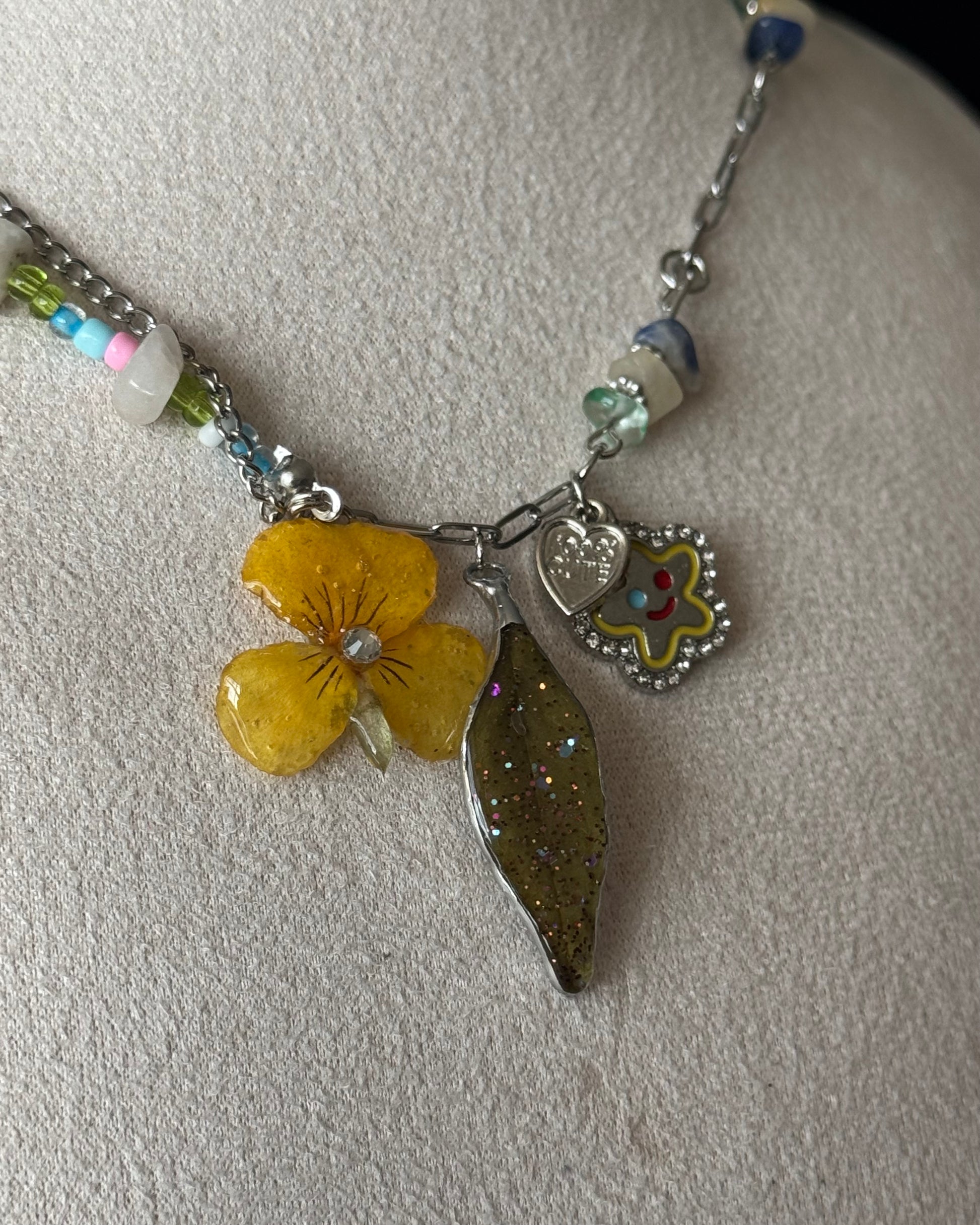 Close-up of preserved yellow pansy and nandina resin pendants with heart charm