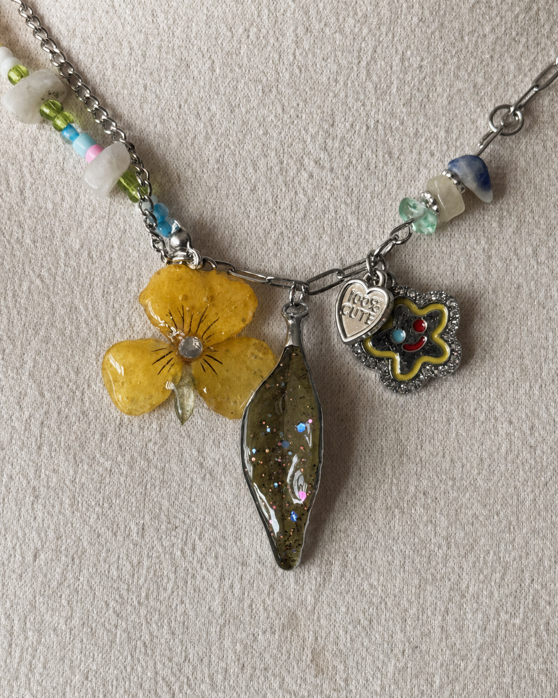 Reflective detail of the botanical pendants and colourful bead pattern, Yellow Pansy & Nandina Leaf Y2K Charm Necklace botanical jewellery by Terra Decode